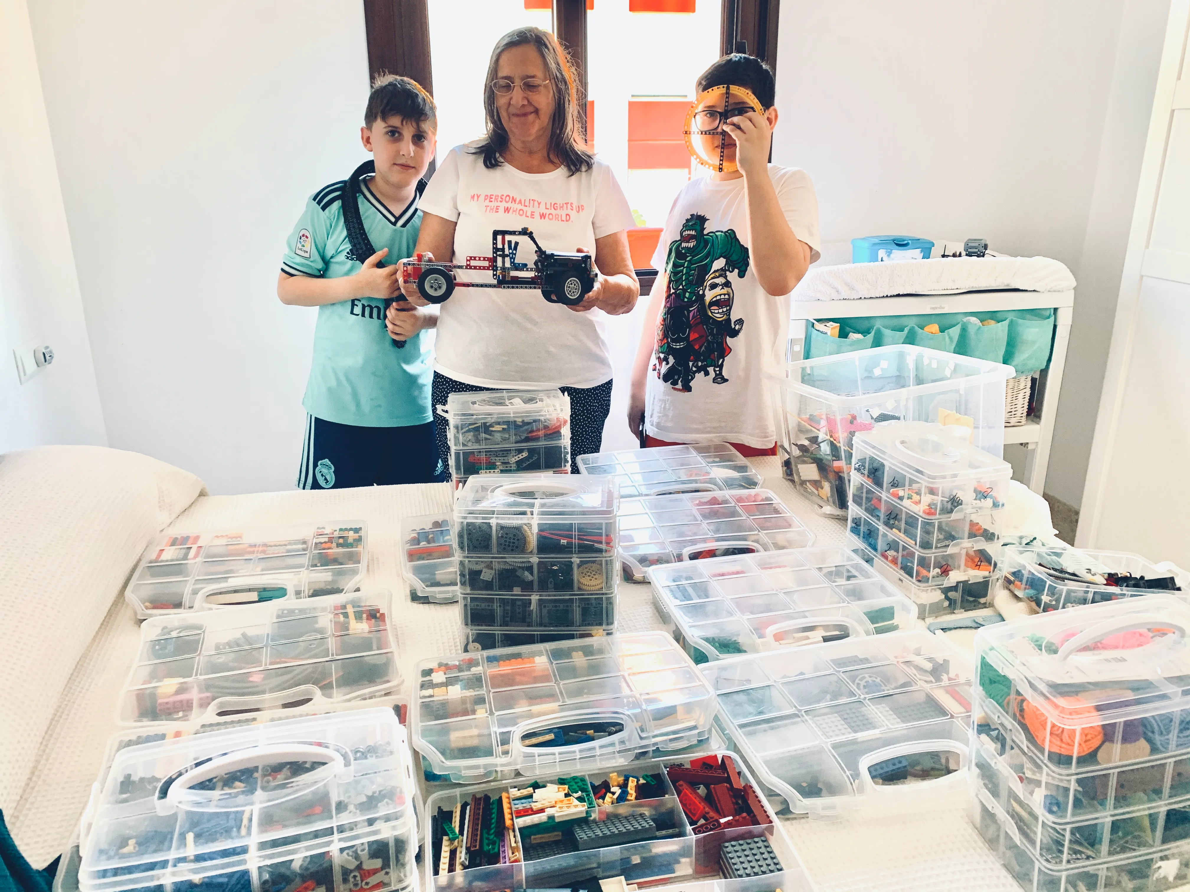 Una mujer y dos niños con un vehículo de LEGO, ante una mesa llena de cajas de piezas clasificadas.