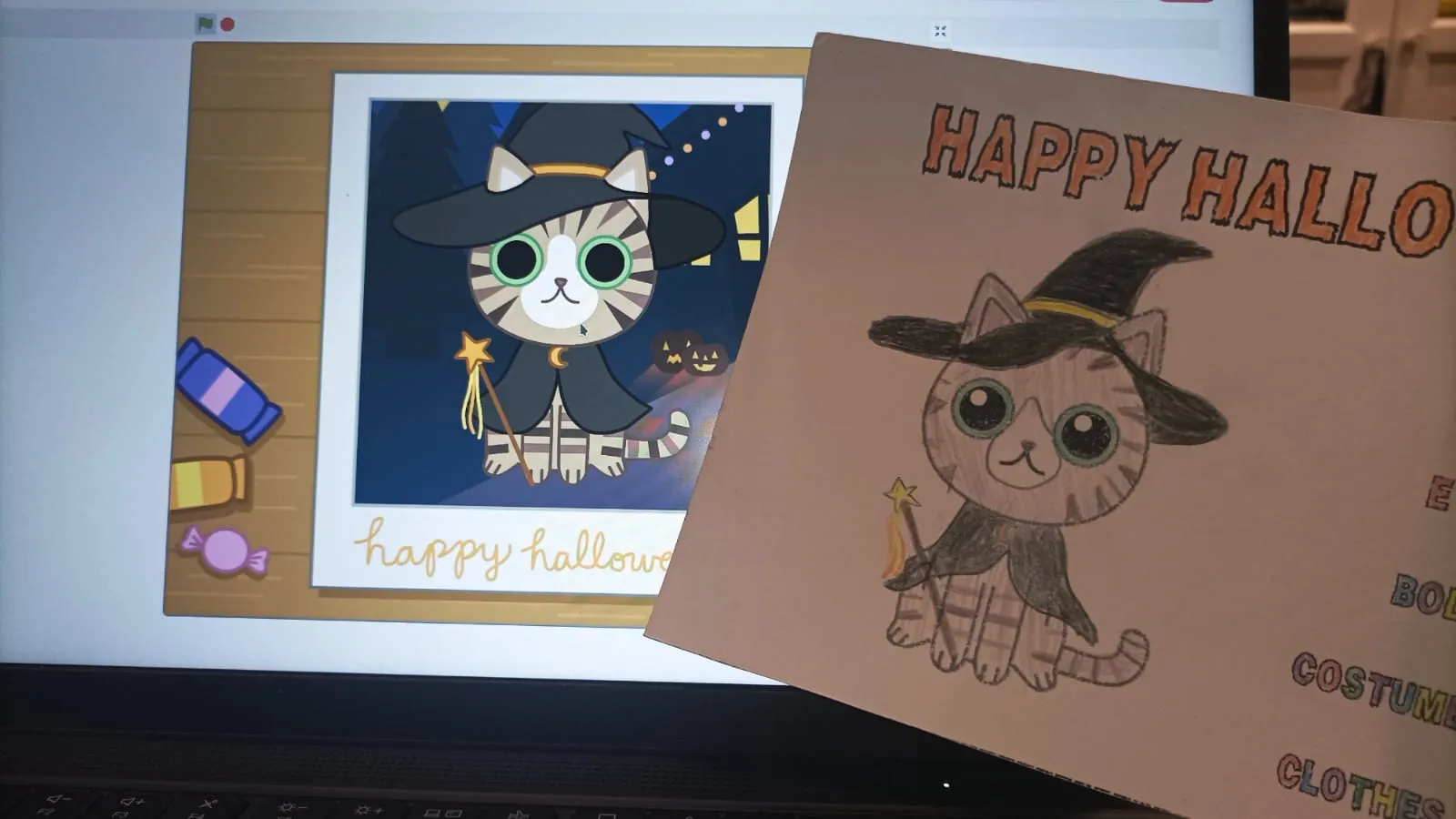 El proyecto en la pantalla del ordenador, con el gato disfrazado, junto a la tarjeta interactiva dibujada por el alumnado.