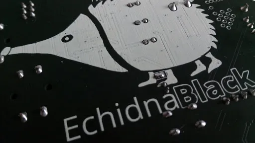 Cara inferior de una placa EchidnaBlack con el dibujo del equidna; entre sus patas delanteras está el puente de soldadura del micrófono.